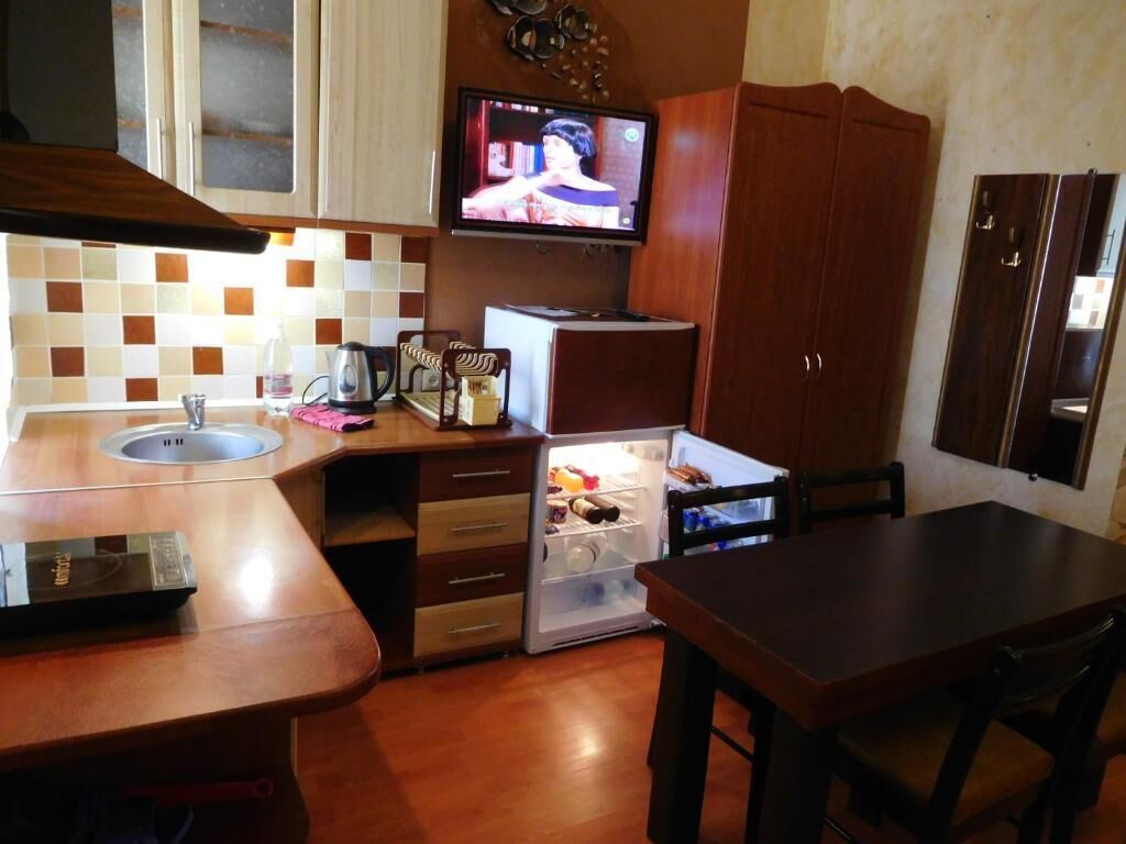 A compact kitchen with a microwave, a small refrigerator, a sink, and a television mounted above the counter.