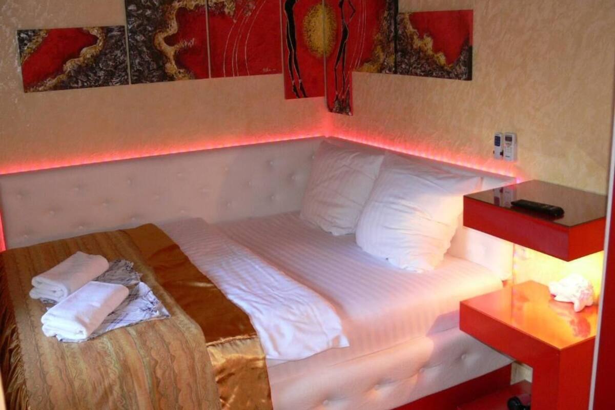 A hotel room with a bed, a red bedside table, and artwork on the wall.
