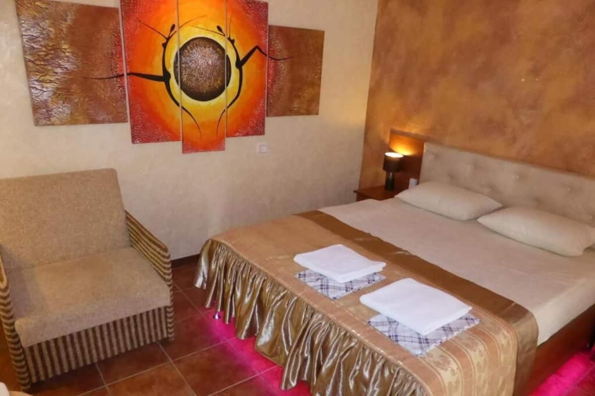 A hotel room with a bed, a chair, and a painting on the wall.