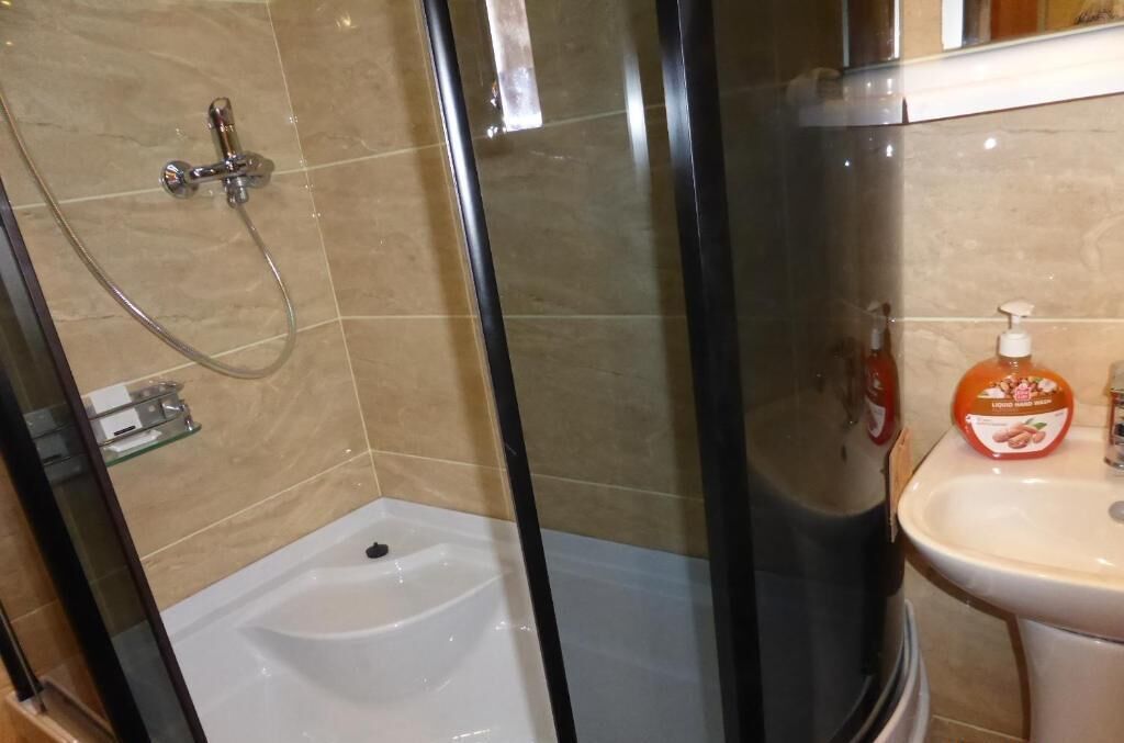 A bathroom with a glass-enclosed shower, a white bathtub, and a sink with a soap dispenser.