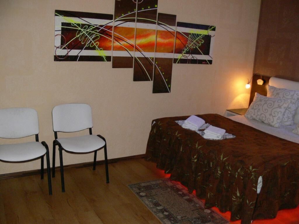 A bedroom with a bed, two chairs, a wall art piece, and a nightstand with a lamp.