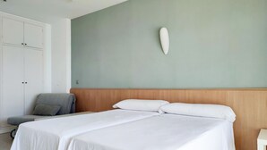 Quarto de hotel com uma cama grande, cabeceira de madeira, uma poltrona cinza e um guarda-roupa branco.