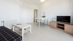 A modern, minimalist room with a bed, a small table, a TV, and a white radiator. - Flats Friends Atlantida 1 bedroom (Benidorm)