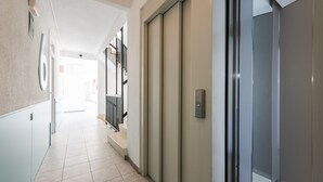A hallway with a tiled floor, a door with a metallic handle, and a staircase with black railings. - Flats Friends Atlantida 1 bedroom (Benidorm)