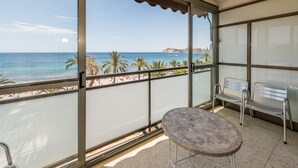 A balcony with a view of the beach, a metal table, and two metal chairs.