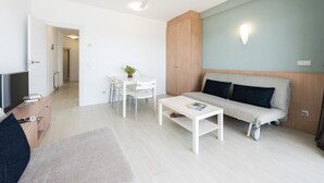 A modern living room with a sofa, a coffee table, a TV, and a dining area with chairs and a table.