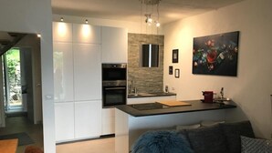 A modern kitchen with white cabinets, a stone backsplash, and a dining area with a blue furry ottoman. - Villetta near Argegno Dizzasco (Muronico)