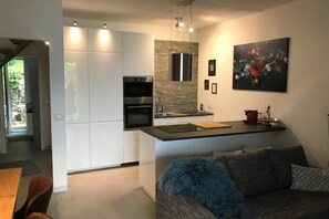 Una cocina moderna con armarios blancos, un protector contra salpicaduras de piedra y una zona de comedor con un otomano azul y mullido.