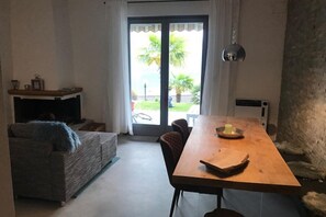 A living room with a sofa, a wooden dining table, and a view through a glass door to a balcony with a palm tree.