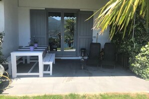 Un patio al aire libre con una mesa y sillas, un ventanal corredero que da a vistas de montañas y una planta en maceta a la izquierda.