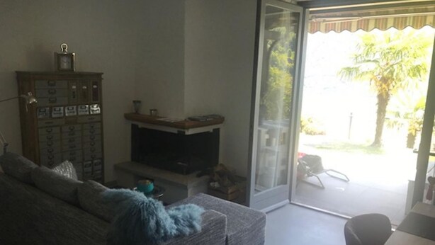 A living room with a sofa, a television, a cabinet, and a sliding glass door leading to an outdoor area. - Villetta near Argegno Dizzasco (Muronico)