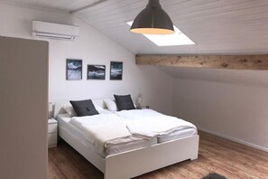 A bedroom with a white bed, a nightstand, a wall-mounted air conditioner, and three framed pictures. - Villetta near Argegno Dizzasco (Muronico)