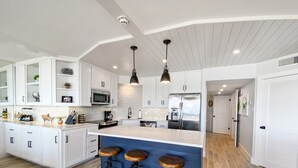 A modern kitchen with white cabinetry, a central island with stools, stainless steel appliances, and pendant lighting. - Sandpiper Condominiums 304, Panoramic Gulf Views w/ direct access to Mustang Island/Port A beaches. (Port Aransas)