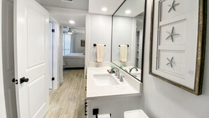 A modern bathroom with a large mirror, two sinks, and a toilet. - Sandpiper Condominiums 304, Panoramic Gulf Views w/ direct access to Mustang Island/Port A beaches. (Port Aransas)