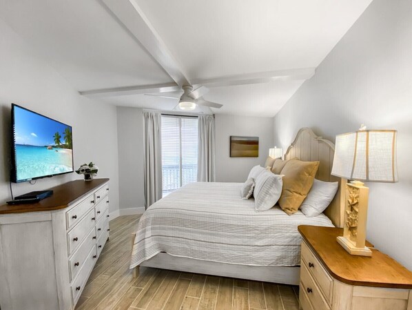 A bedroom with a bed, a TV, a ceiling fan, a nightstand, and a window with curtains.
