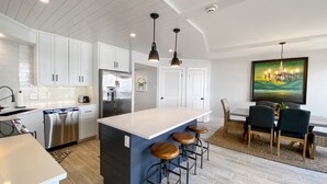 Una cucina moderna con mobili bianchi, un frigorifero in acciaio inossidabile, una grande isola con sgabelli da bar e un'area pranzo con tavolo e sedie.