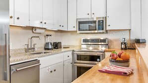 A modern kitchen with white cabinets, stainless steel appliances, a microwave, a coffee maker, and a fruit bowl on the counter. - Summer in Snowmass! Spacious Condo w/ Sleeping Den, Pool, Hot Tub, Balcony W/ Grill, FP & Parking (Snowmass Village)
