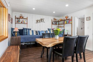 A cozy room with a wooden dining table, black chairs, a blue sofa, and bookshelves filled with books and decorative items.