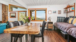 A cozy room with a wooden dining table, black chairs, a sofa, and a bed. There are large windows offering a view of the outdoors. - Summer in Snowmass! Spacious Condo w/ Sleeping Den, Pool, Hot Tub, Balcony W/ Grill, FP & Parking (Snowmass Village)