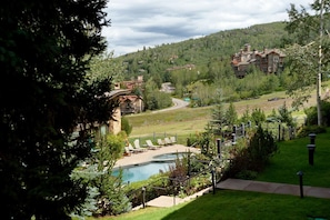 A resort with a pool, lounge chairs, and a view of a ski lift and buildings in the distance.