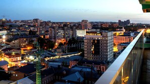Une vue sur la ville au crépuscule, avec des bâtiments illuminés et une grande grue verte bien visible.