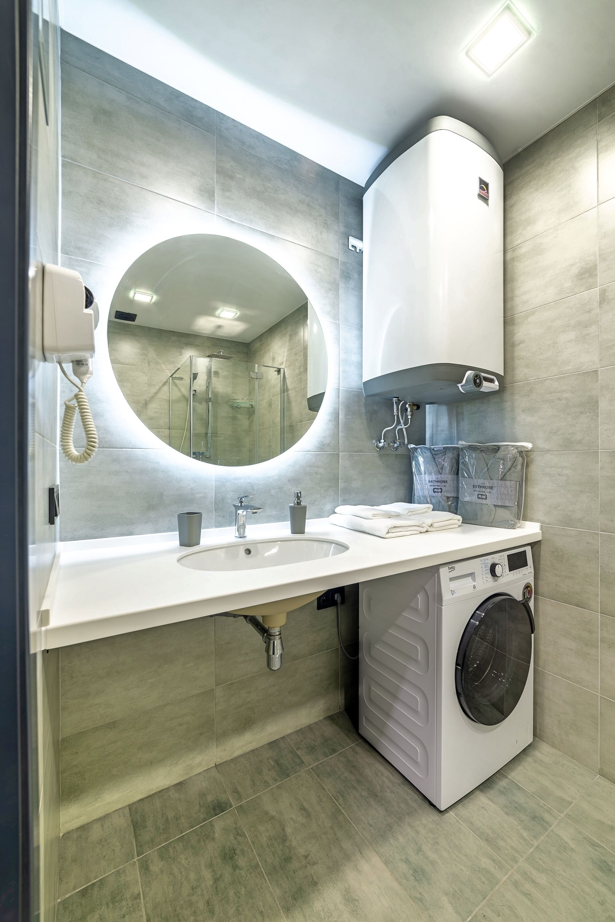 A modern bathroom with a large mirror, two sinks, a washing machine, and a towel dispenser.