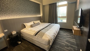 Una habitación de hotel moderna con una cama grande, un televisor de pantalla plana, una mesita de noche y una ventana con cortinas.