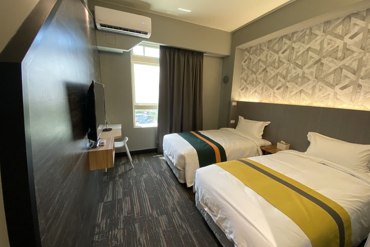 Habitación de hotel con dos camas, un escritorio con silla, televisión y aire acondicionado.