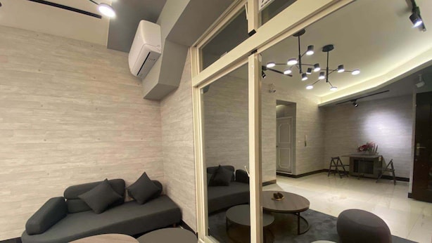 Una sala de estar moderna con un sofá gris, dos mesas redondas y un separador de vidrio.
