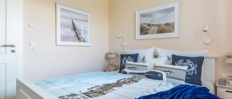 A bedroom with a bed, two bedside tables, a nightstand, a wall-mounted lamp, and two framed pictures.