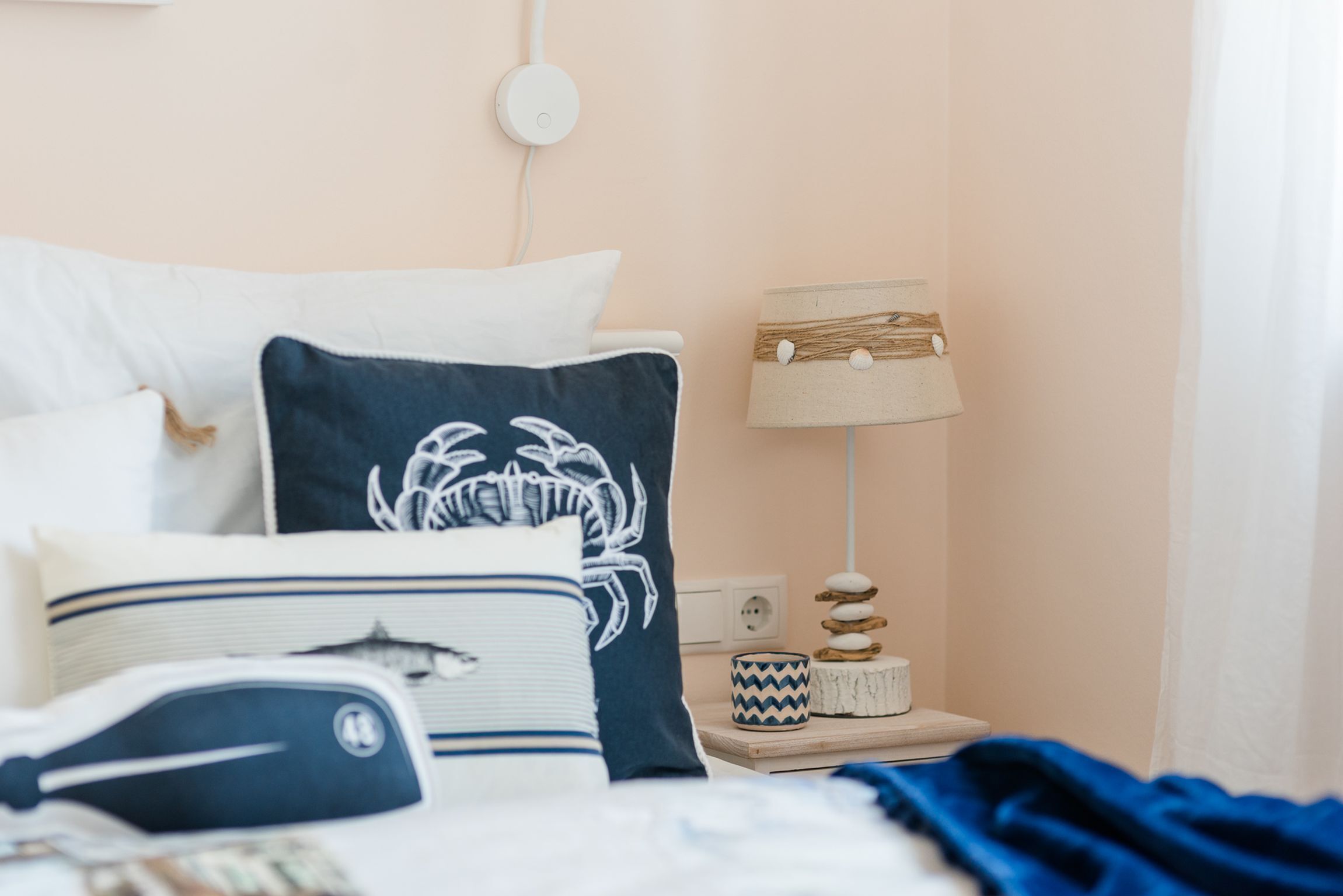 Ein ordentlich eingerichtetes Schlafzimmer mit Bett, Kissen, einem Nachttisch mit Lampe und einer Wandsteckdose.