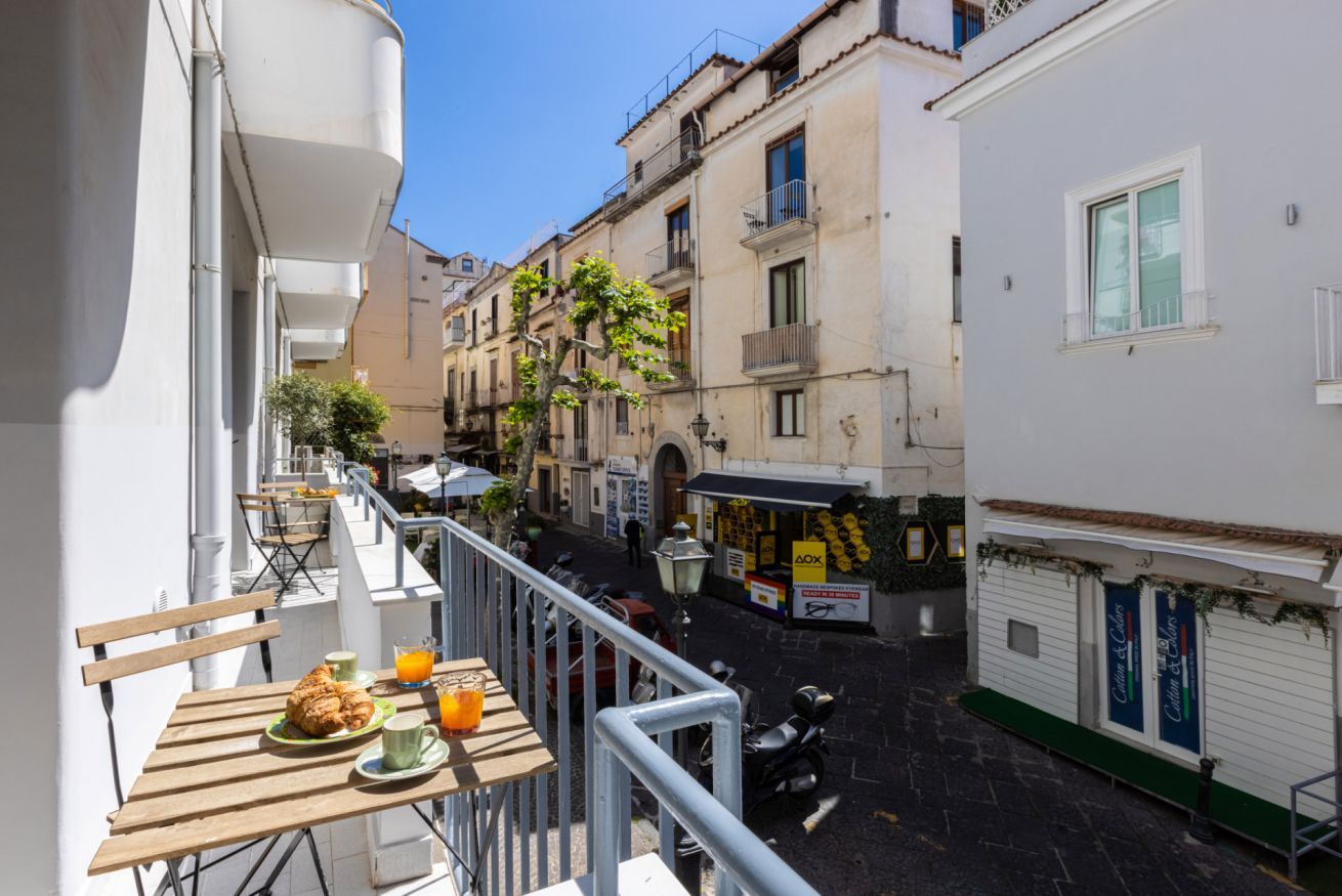 A narrow street with buildings on either side, a café with outdoor seating, and a parked scooter.