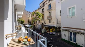 A narrow street with buildings on either side, a café with outdoor seating, and a parked scooter.