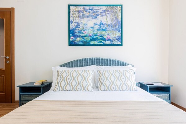 A bedroom with a bed, two nightstands, a painting, and a door.
