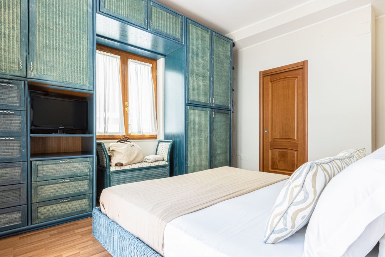 Une chambre à coucher avec un lit, une fenêtre avec des rideaux, une porte en bois et une armoire à plusieurs compartiments.