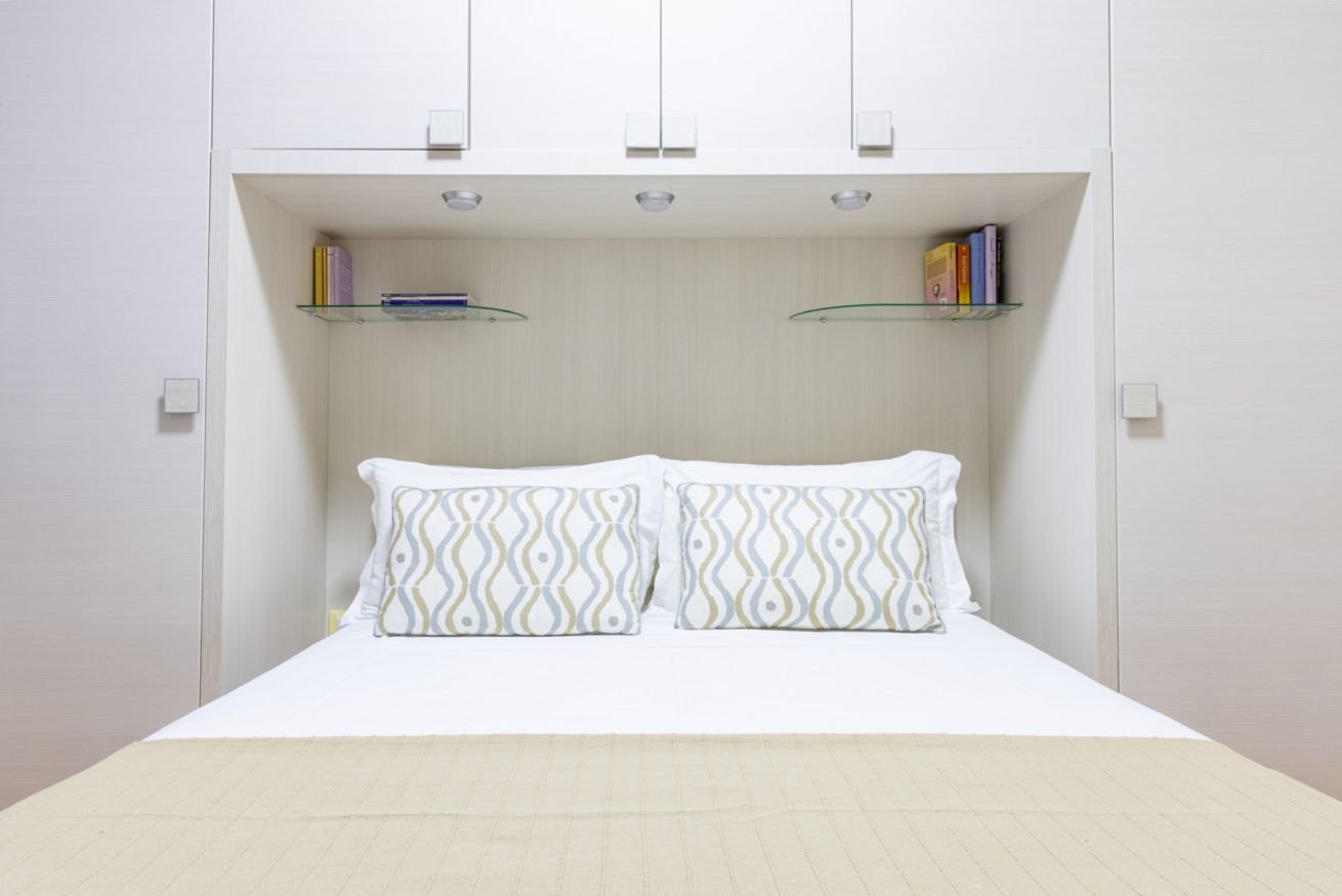 A bedroom with a bed, two pillows, and two shelves with books.