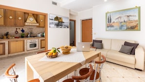 A modern kitchen with wooden cabinets, a dining table with chairs, a laptop, and a painting on the wall.