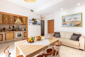 A modern kitchen with wooden cabinets, a dining table with chairs, a laptop, and a painting on the wall.