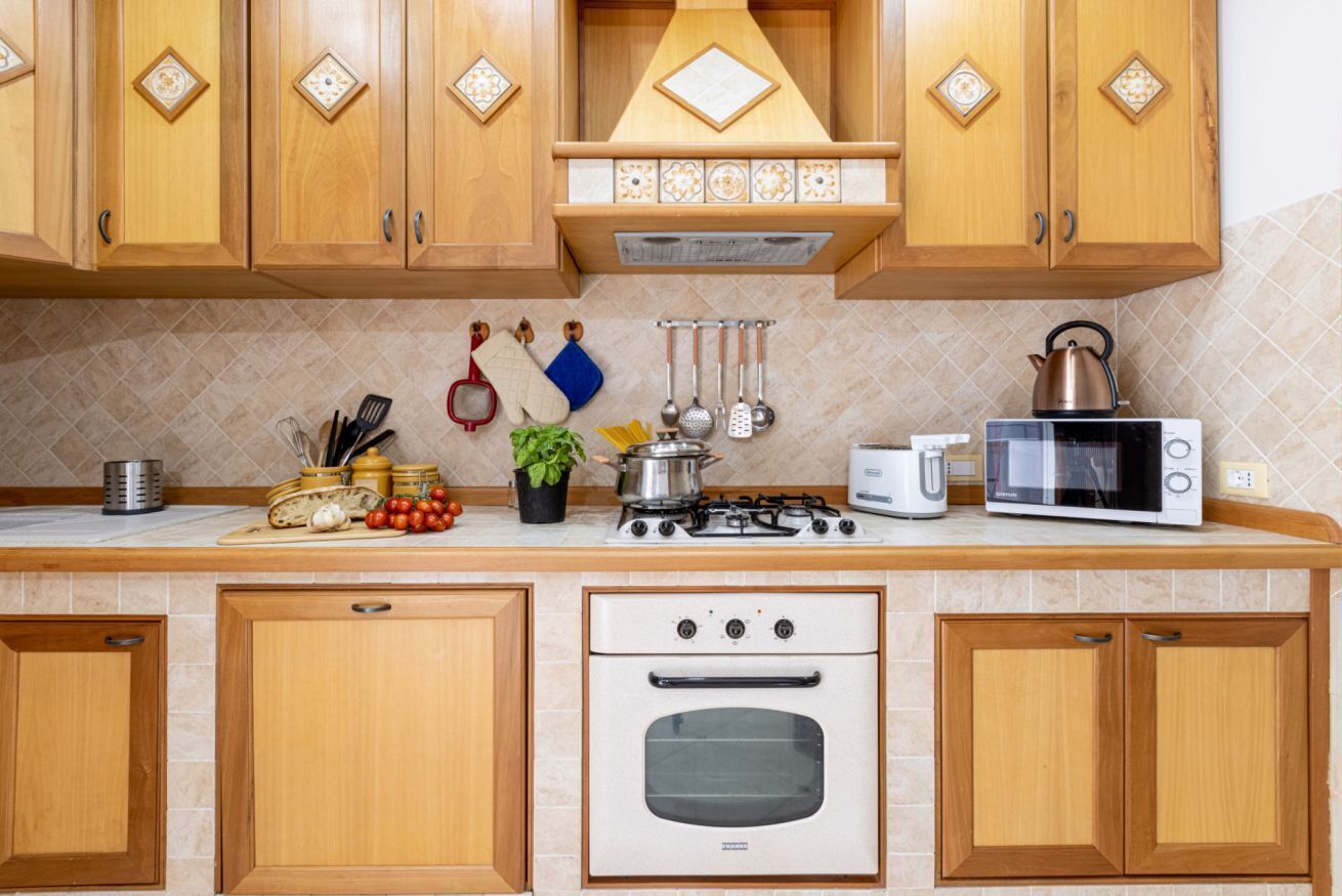 Una cucina con mobili in legno, un fornello a gas, un forno a microonde e diversi utensili da cucina.