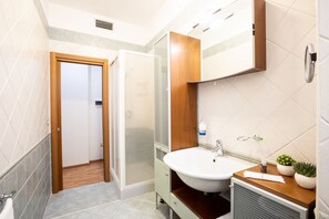 A bathroom with a wooden vanity, a sink, a mirror, and a shower area.