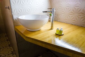 Un baño con un lavamanos blanco de diseño, un grifo cromado y dos pequeñas botellas de jabón líquido sobre una encimera de madera.