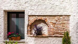 Un mur de briques rustique avec une fenêtre, une petite étagère ornée de plantes en pot et un sol carrelé.