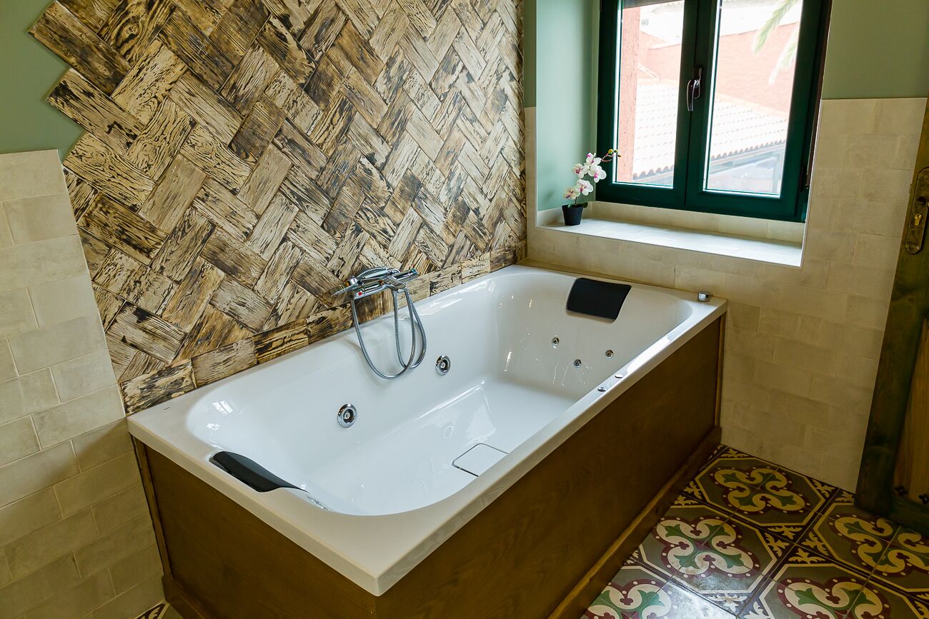 Un baño con una bañera grande, pared con diseño de espiga, pequeña ventana con vistas y baldosas de suelo estampadas.