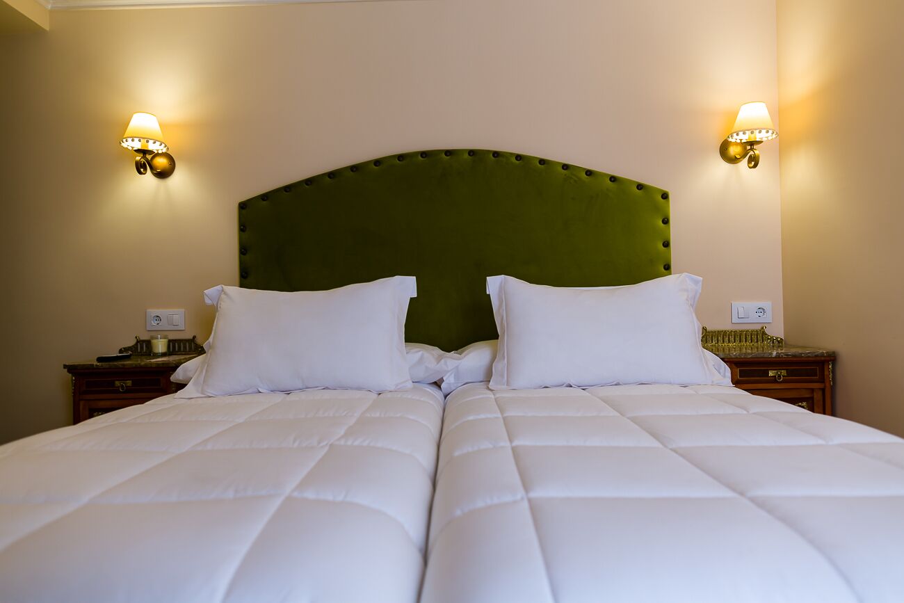 Una cama doble con un cabecero tapizado en verde, dos mesitas de noche con lámparas y una pared de color neutro.