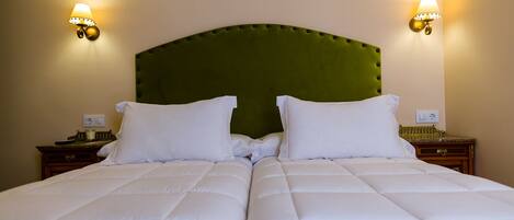 Una cama doble con un cabecero tapizado en verde, dos mesitas de noche con lámparas y una pared de color neutro.