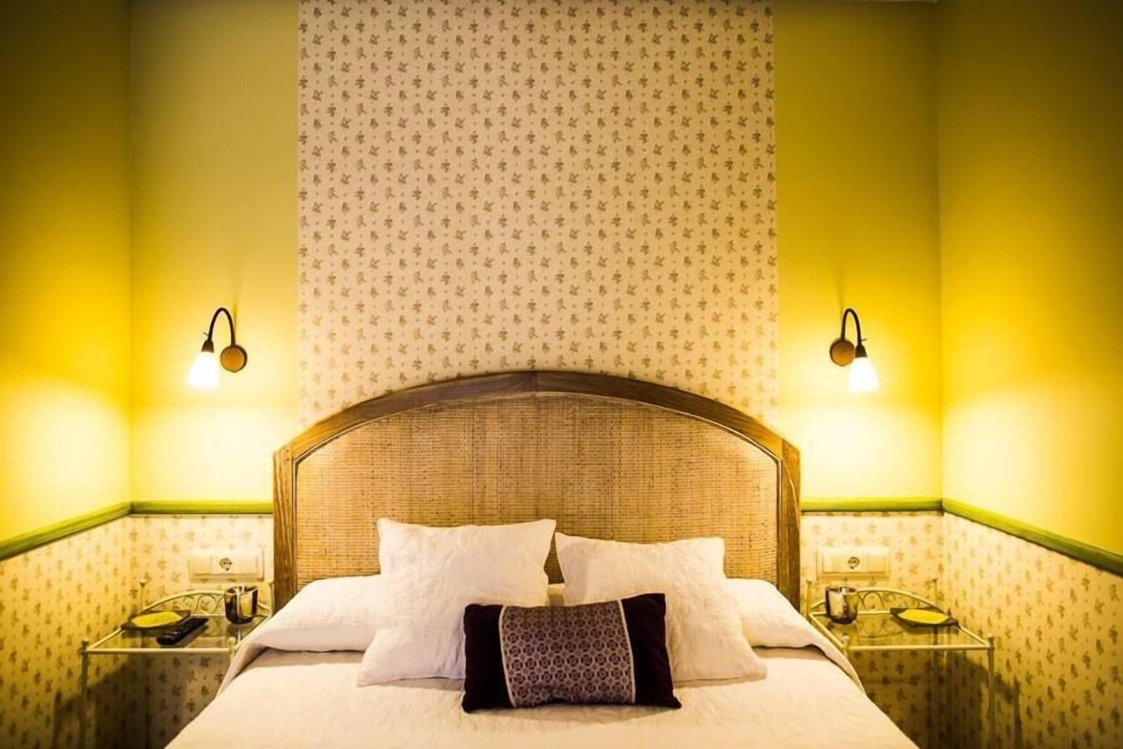 A hotel room with a large bed, two bedside tables, and a patterned wallpaper.