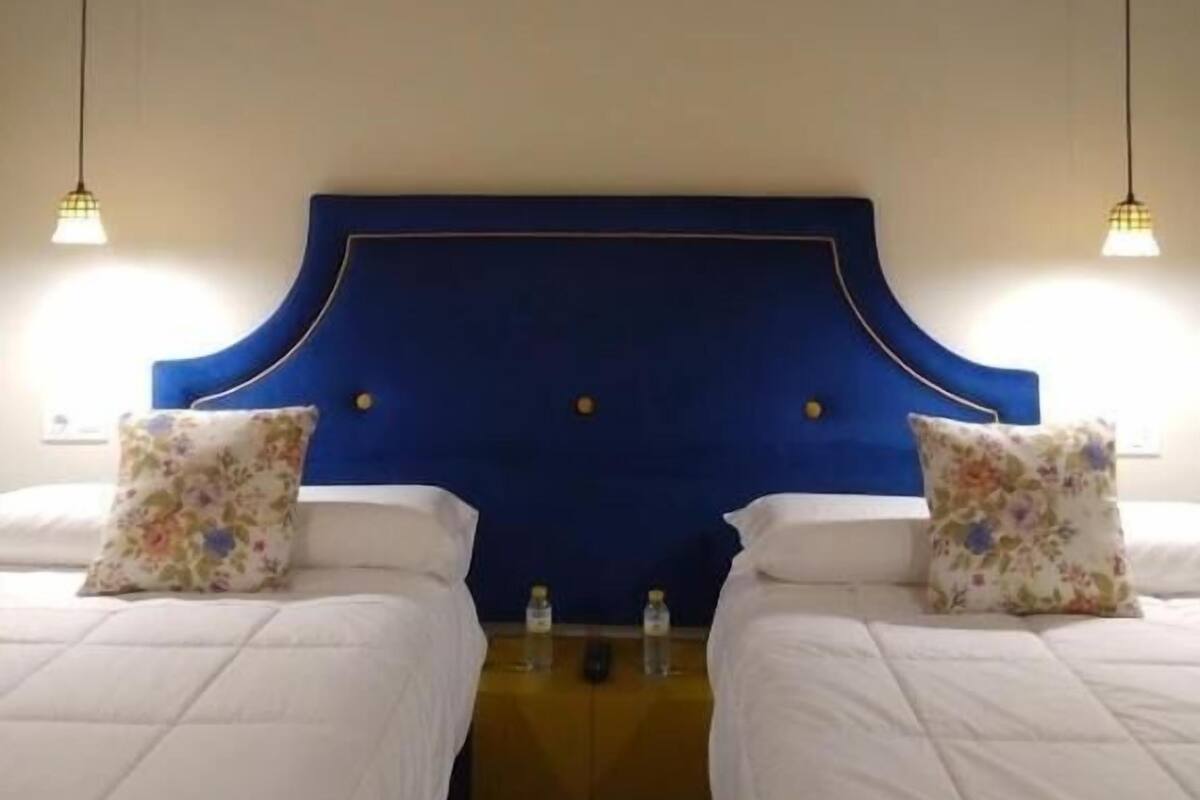 Un dormitorio con dos camas, techo de madera y cabecera azul.