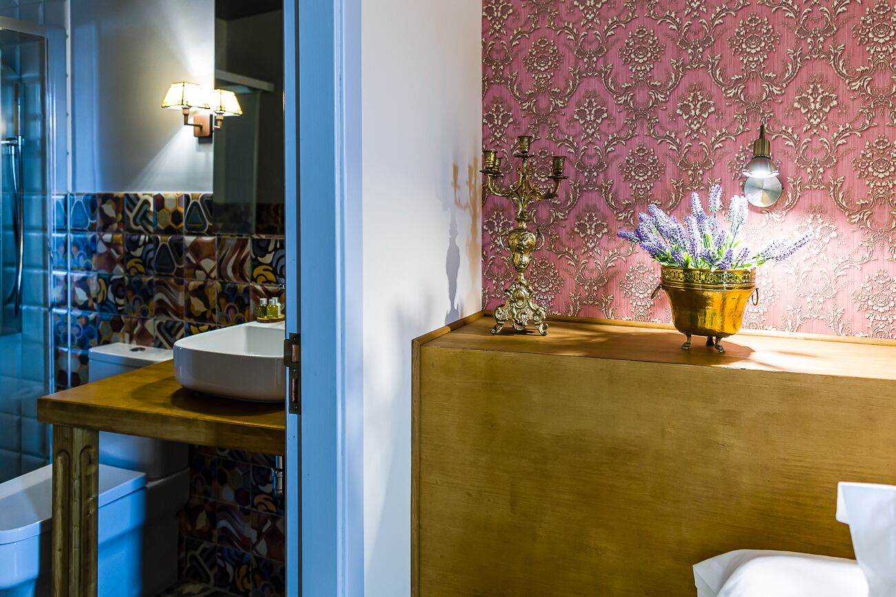 A bathroom with a white sink, a mirror, a patterned wall, and a decorative candelabra with a potted plant.