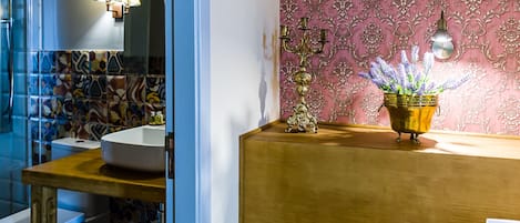 A bathroom with a white sink, a mirror, a patterned wall, and a decorative candelabra with a potted plant.