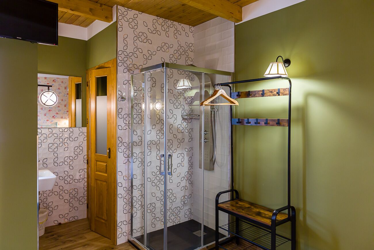 Une douche avec une porte en verre, un banc en bois et une lampe fixée au mur.